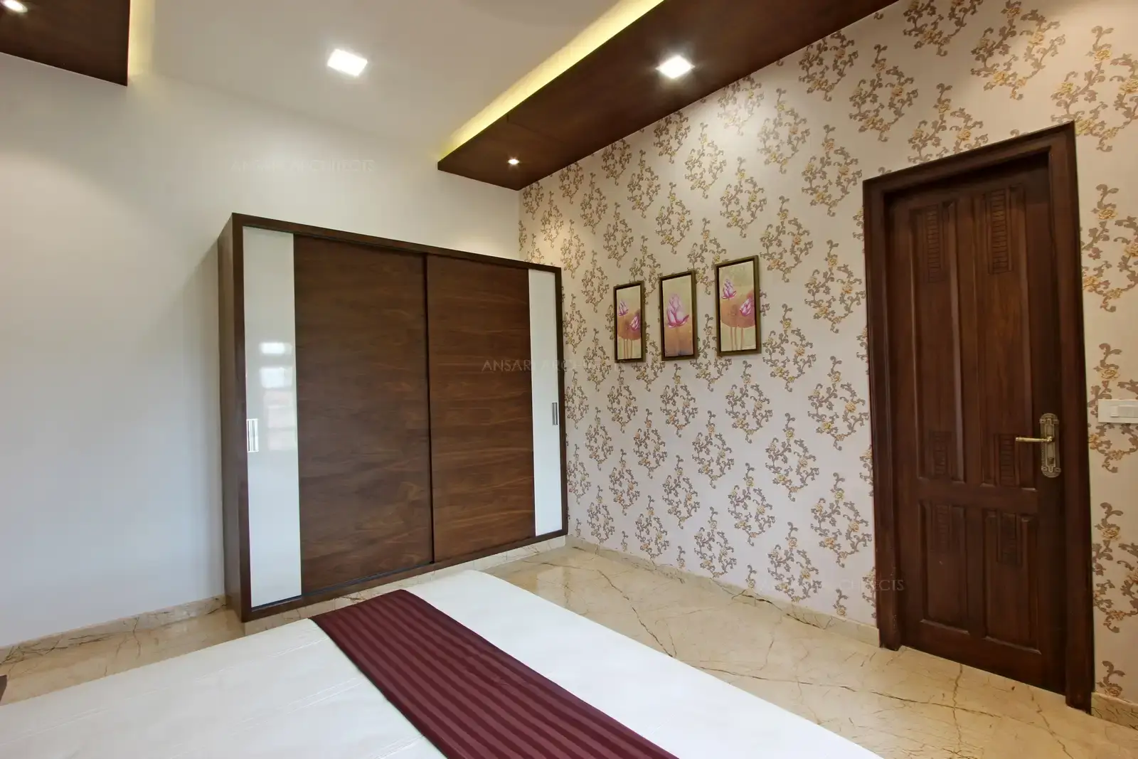 The bedroom with selected wallpaper finish and royal veneer finish highlights along with the lighting. Wardrobe is simple and adds more complement to the space.