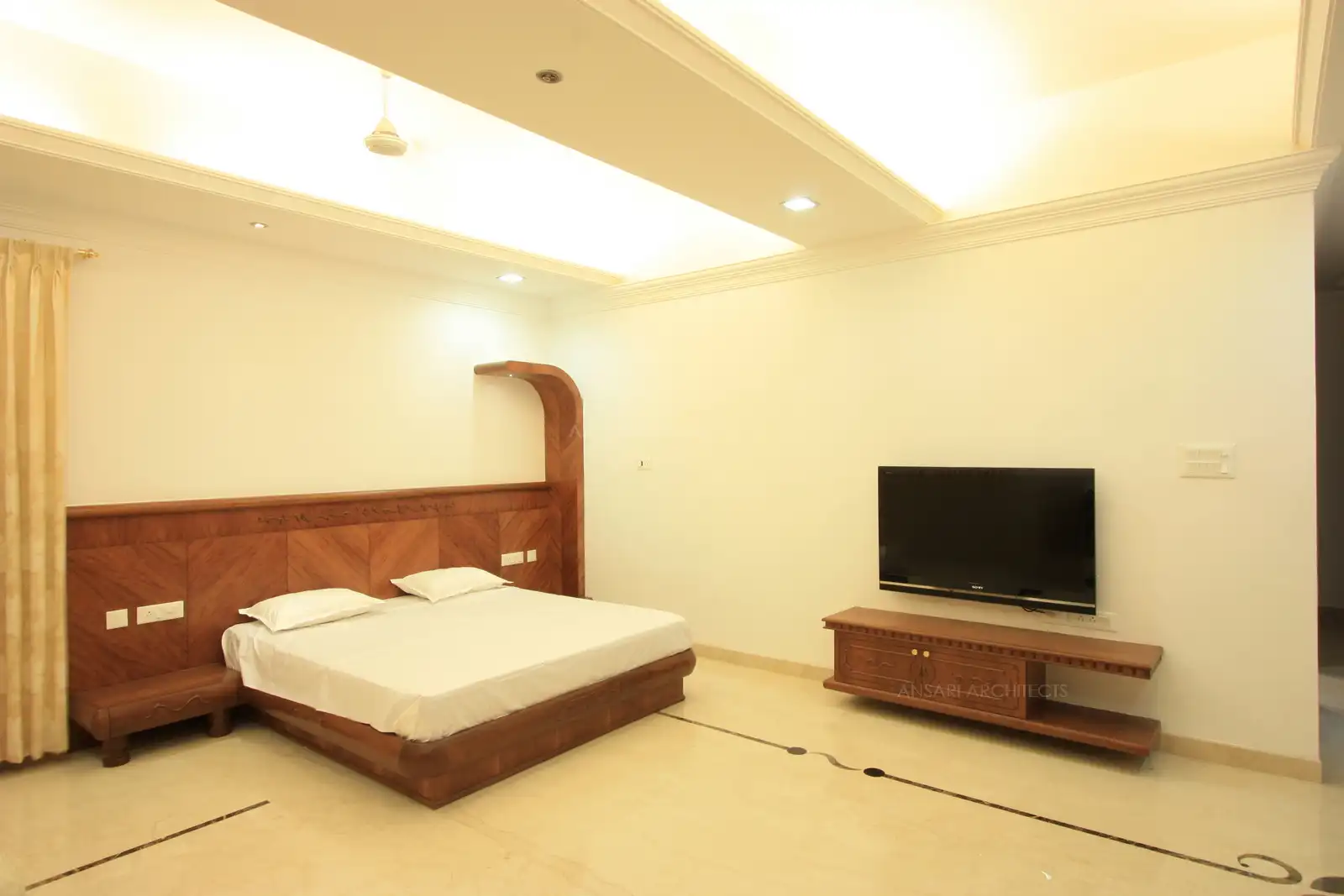 Guest bedroom-1 looks spacious with simple bedhead and a TV unit.