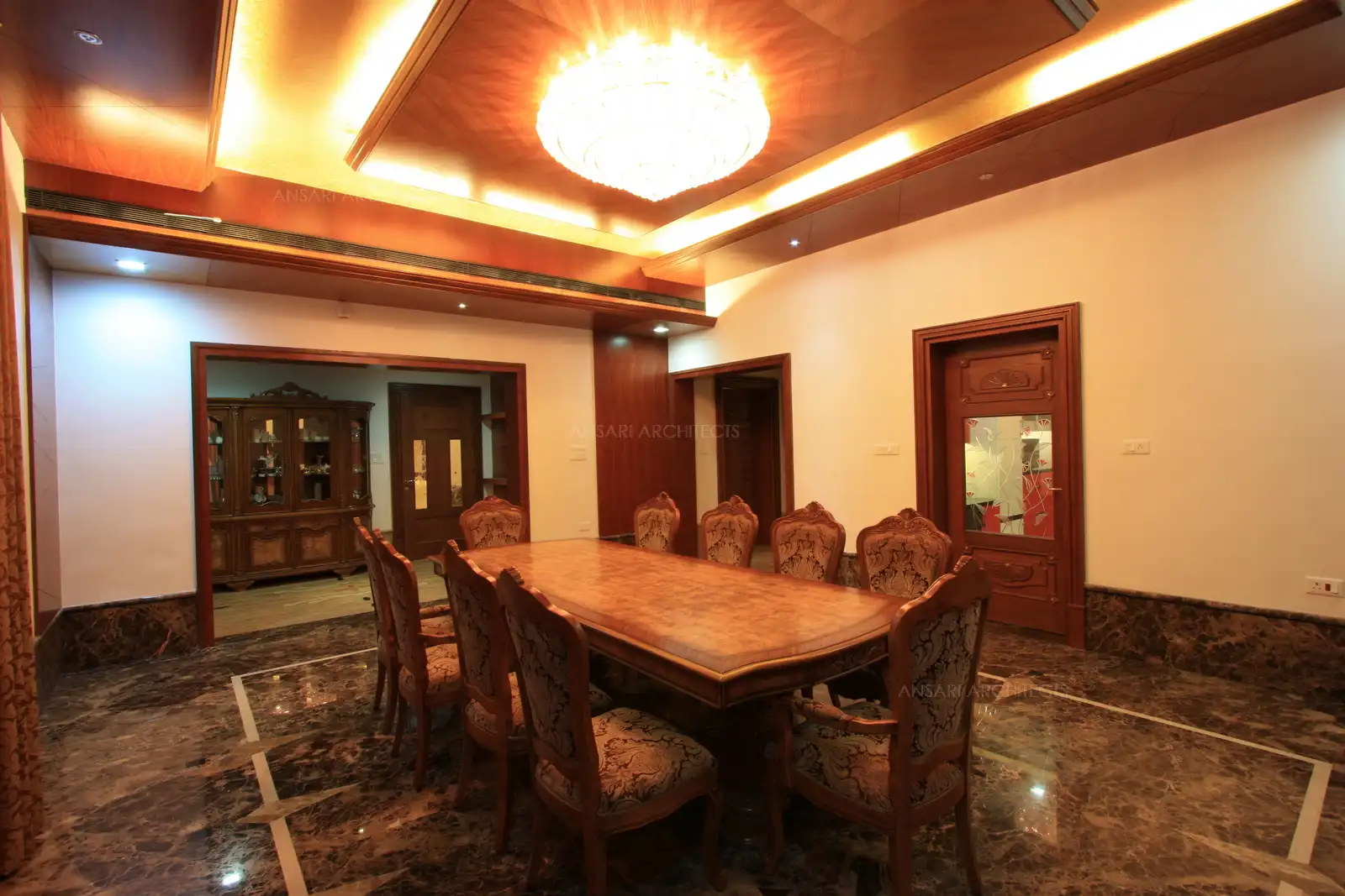 Informal dining room used by the family has a posh dining table with wooden false ceiling and chandlier above.