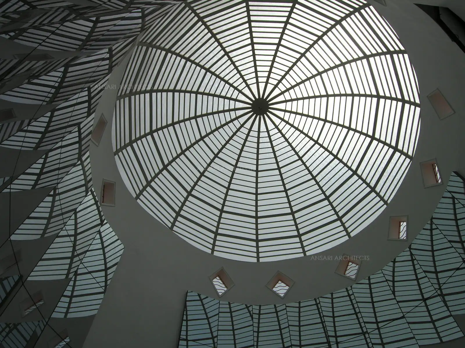Modern architectural dome with geometric glass and metal patterns, reflecting light in a symmetrical design. Interior view showcasing unique curves and angles.