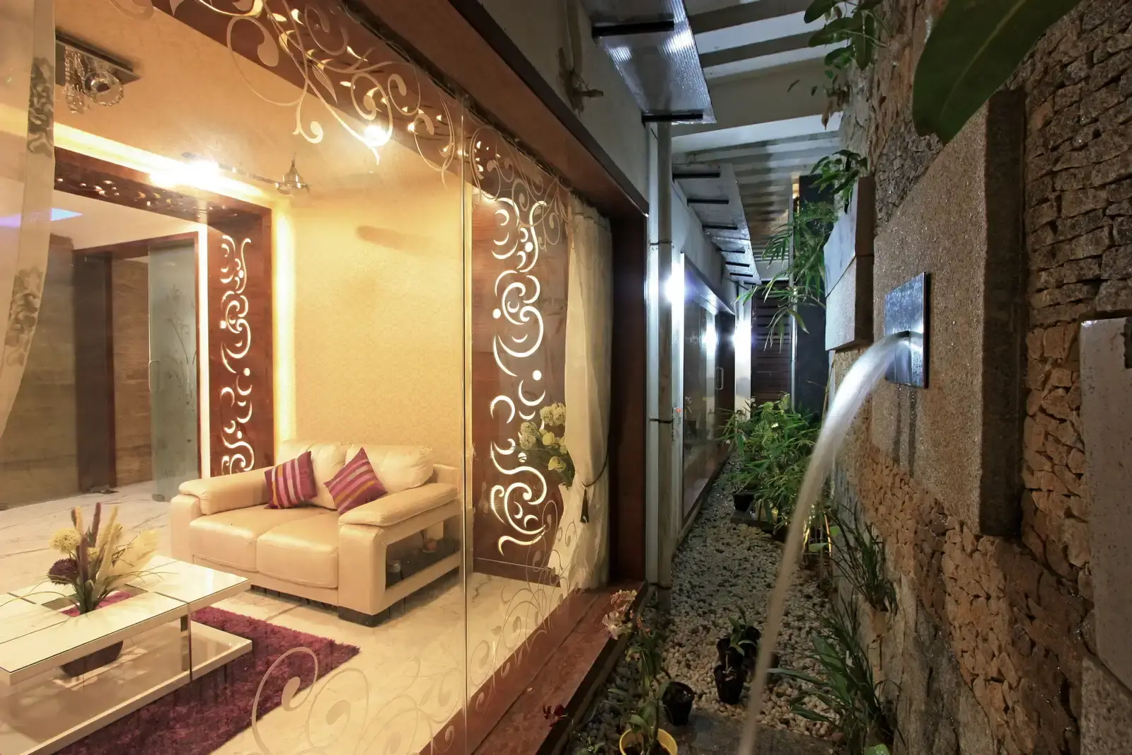 A courtyard designed with rustic natural stones, bebble flooring, water feature and plants covered with pergolas add natural lights to the indoors with an aesthetic view.