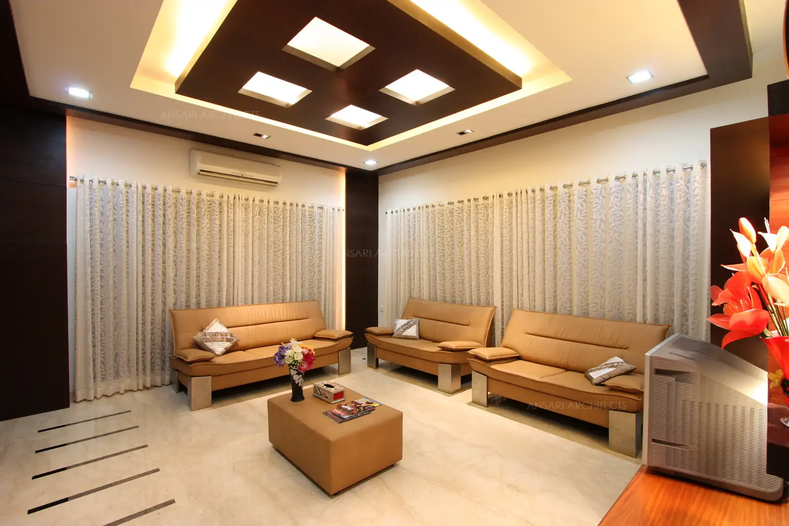 Large windows draped with elegant white curtain merges with the wall creating an interesting look to the L shape wall in this drawing room.