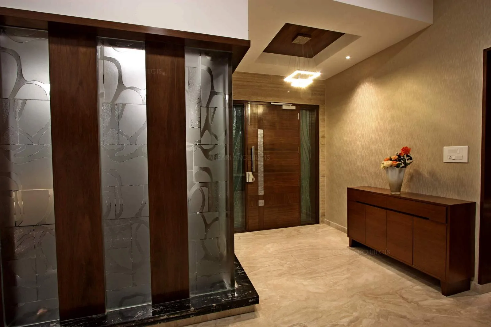 The foyer exudes drama, numerous materials tie in together, from the frosted glass with abstract patterns, the wallaper feature wall, the marble flooring to the woodwork and the beautiful light hung from a recessed ceiling offers a refreshing appeal.