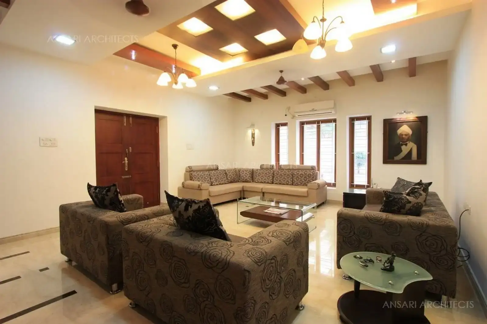 This angle shows the main door and the corner sofa Seating, which contrasts in colour with the rest of the dark Seating, and the glass teapoy adds a contemporary touch to the Melange 