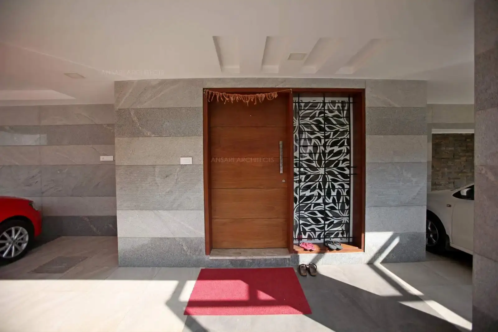 The entrance door is a contemporary finish with stone cladding on the exterior walls along with full length window and decorative pattern. Dark wood finish is highlighted for the door with recessed lights on the ceiling.