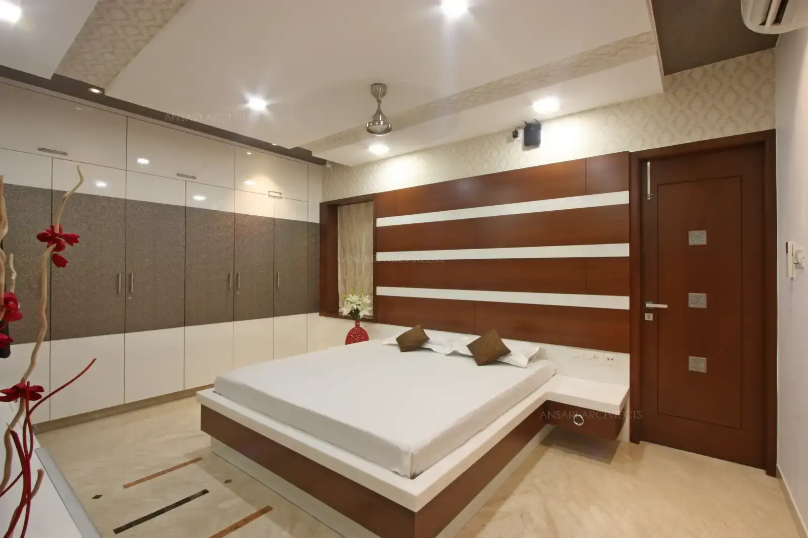 The wardrobe unit is defined by clean lines and solid blocks of striking grey tones. The space features headboard with veneer panelling and seamless white strips remains as a focal point.