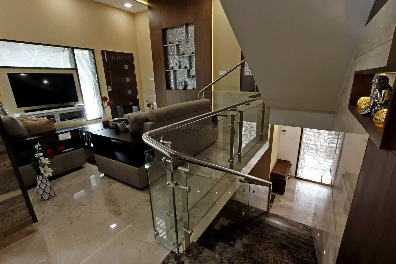 Puntured niches in dark wood with mirror insets highlight the space with a brighter hue acts as a centre of attraction. Adding to accessories is a good touch of artistry with buddha sculpture in the staircase wall with lights add more depth with the panelling behind.