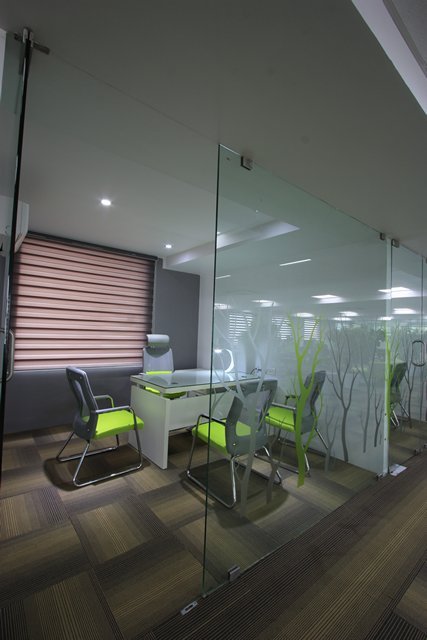 Glass-walled meeting room with frosted tree motifs, vibrant green seating, white desk, and patterned flooring