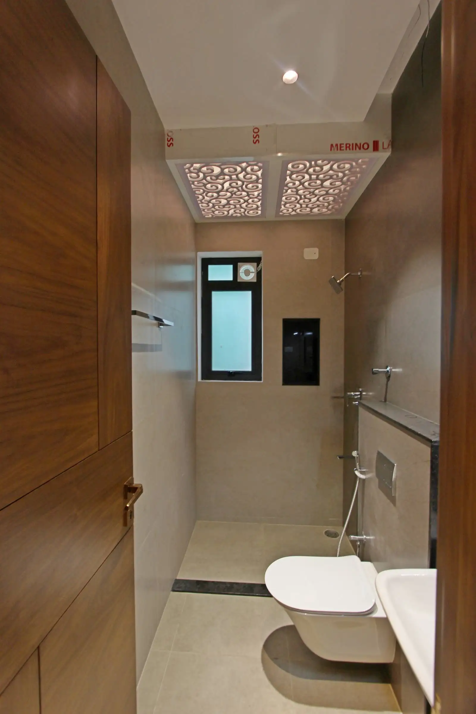 The bathroom features a modern minimalist design with beige tiles, sleek fixtures, and patterned ceiling panels, combining functionality with subtle decorative elements.