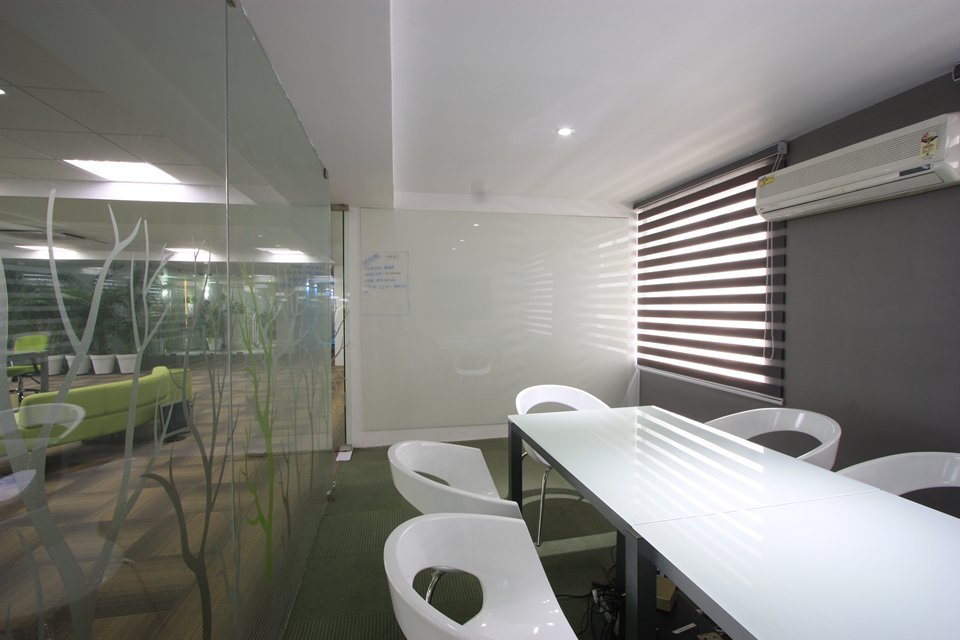 Conference room featuring a sleek table, minimalist seating, decorative glass partition, striped blinds, and integrated climate control for a refined, functional space