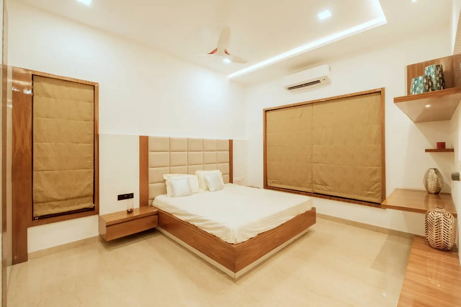 Minimalist bedroom with symmetrical wood-framed windows, beige Roman blinds, and warm wood finishes, blending natural light and modern design.

