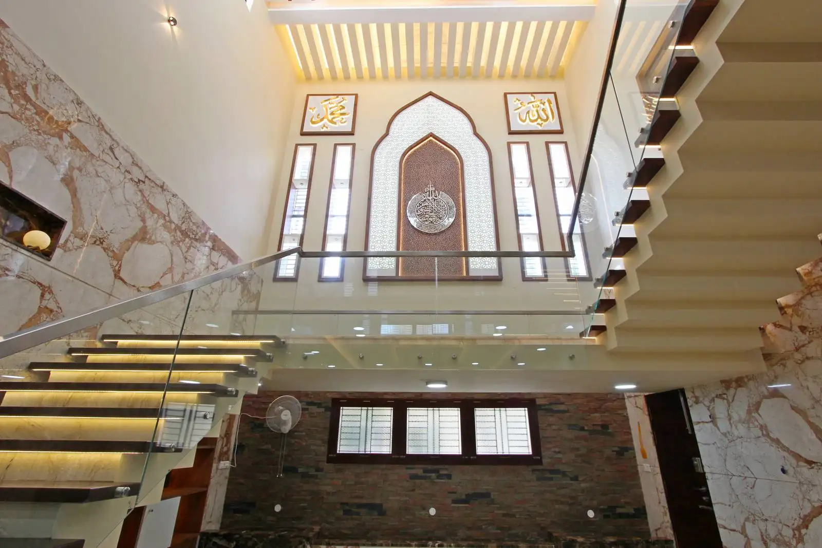 The staircase is a prominent architectural feature, with floating treads and integrated lighting. The use of glass balustrades enhances transparency and allows natural light to flow through the space, creating an open and airy feel.