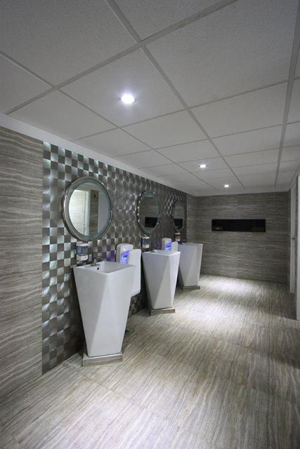 Restroom with textured walls, round mirrors, and bright lighting for a functional, inviting space. Durable materials and thoughtful layout enhance comfort and maintenance.