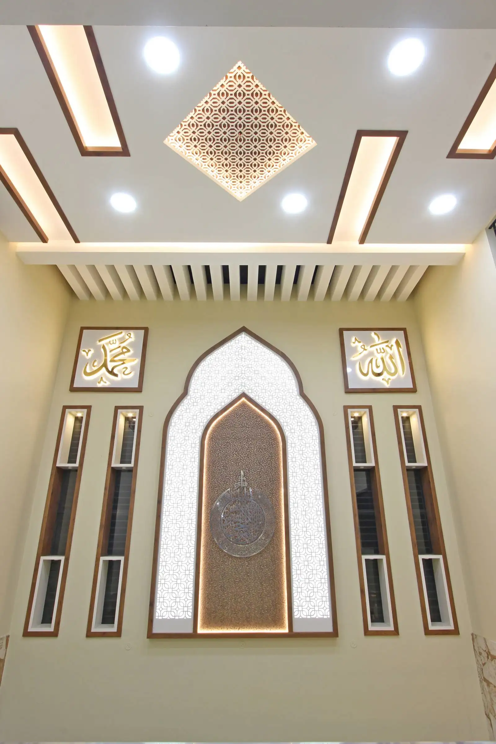 The area features a dramatic double-height ceiling, which adds grandeur and vertical spaciousness. The upper wall is adorned with Islamic calligraphy and a decorative niche, serving as a focal point and infusing cultural identity into the design.