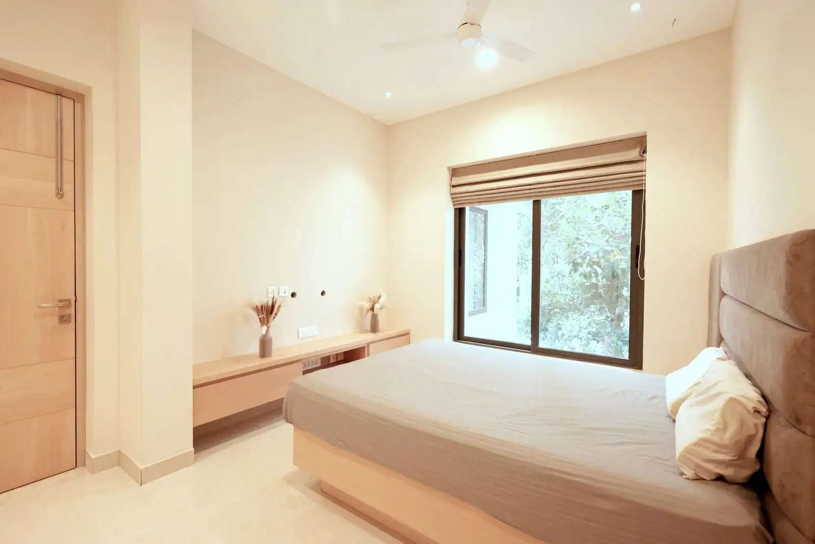 A large window with a Roman blind brings in ample natural light and ventilation, visually opening up the space while framing views of the surrounding greenery.