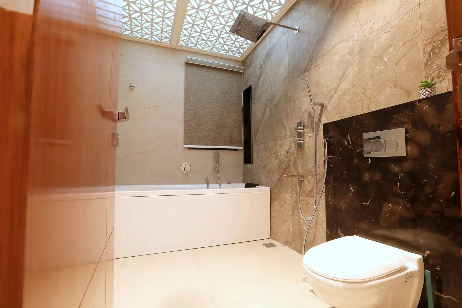 Elegant bathroom featuring light beige marble walls, a white bathtub, handheld shower, and dark marble accent wall with integrated storage and greenery.