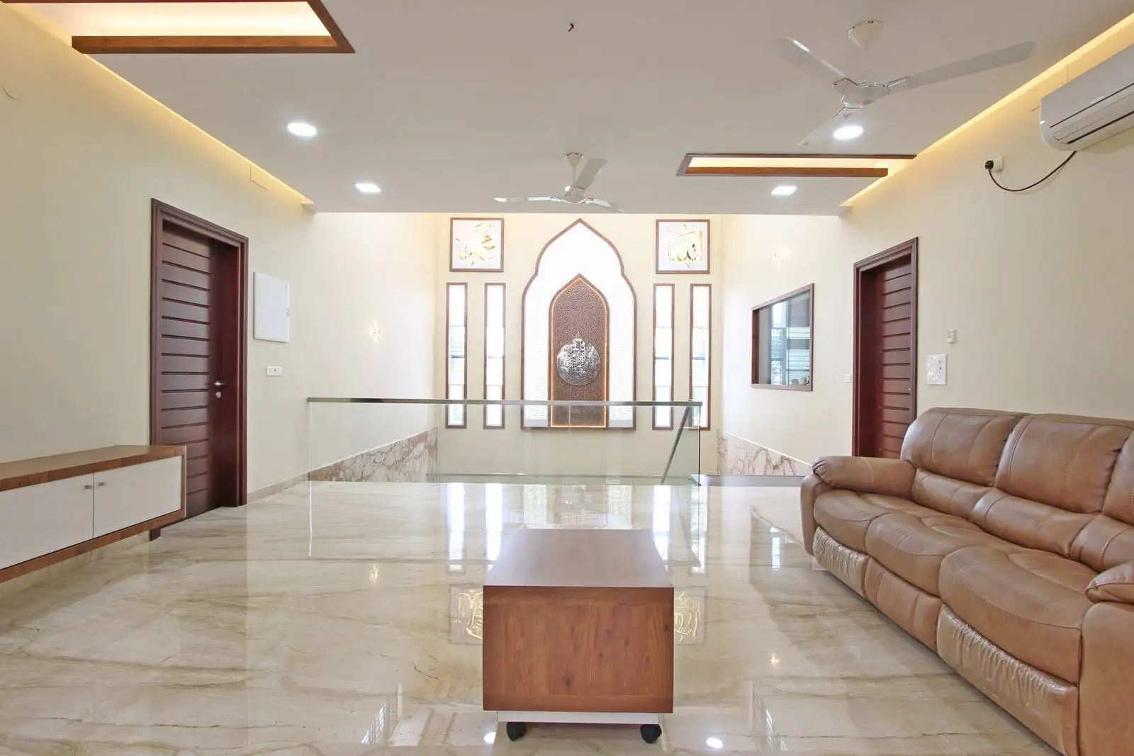 A spacious first-floor family lounge with a symmetrical layout, central glass-balustrade staircase, and simple leather sofa seating, offering openness and easy flow between floors.