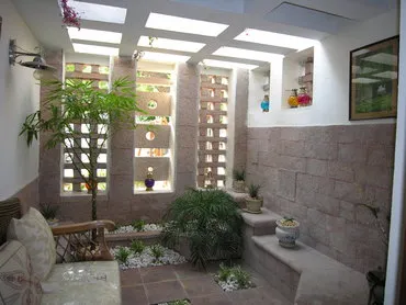 Indoor patio with skylights, featuring plants, a stone bench with potted plants, and a window with a framed picture on the wall.