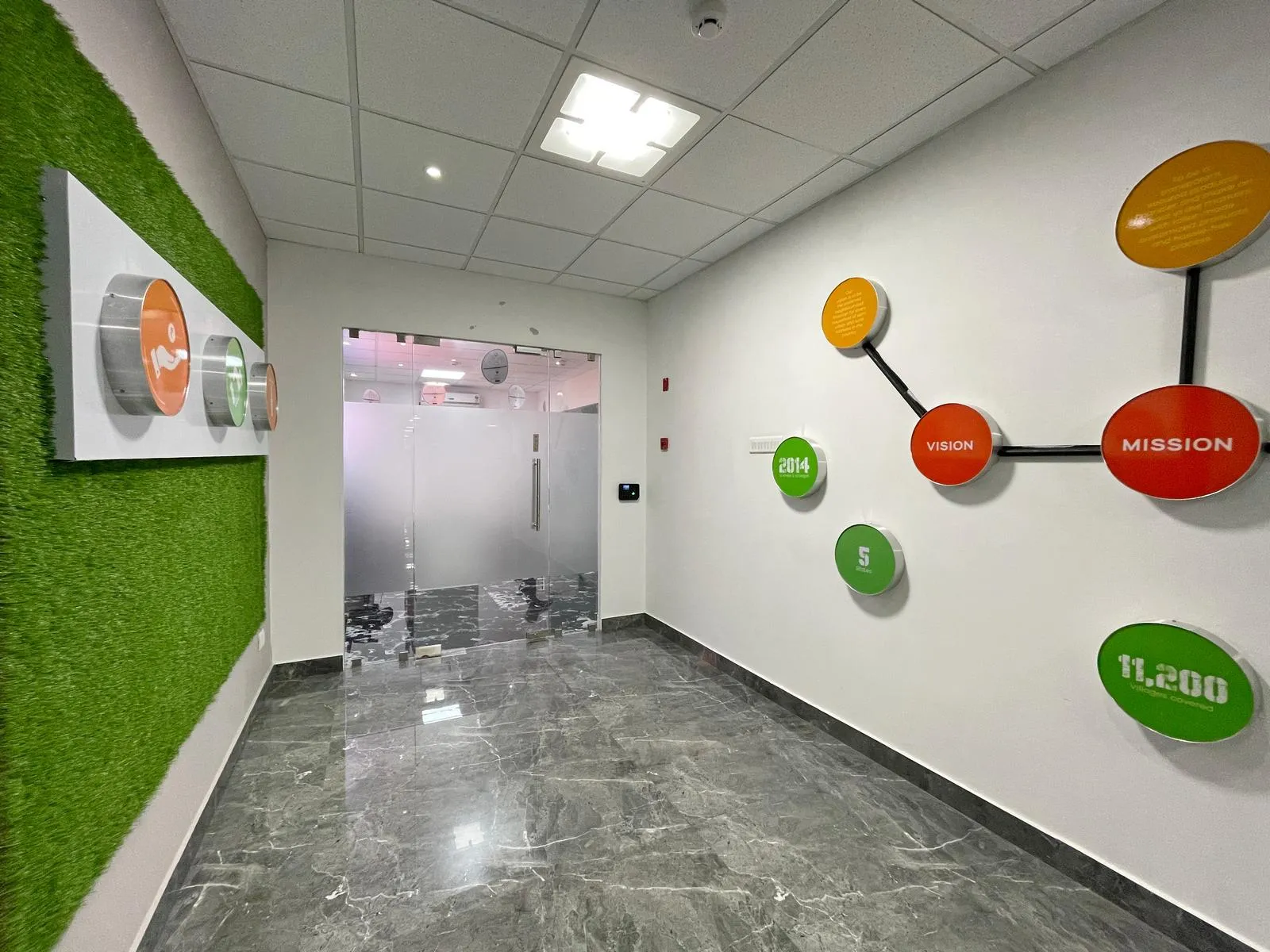 Corridor blends polished marble flooring, suspended ceilings, and branded installations to create a visually engaging transitional space. Feature walls, acrylic panels, and integrated lighting enhance brand storytelling, spatial clarity, and a modern, professional aesthetic.