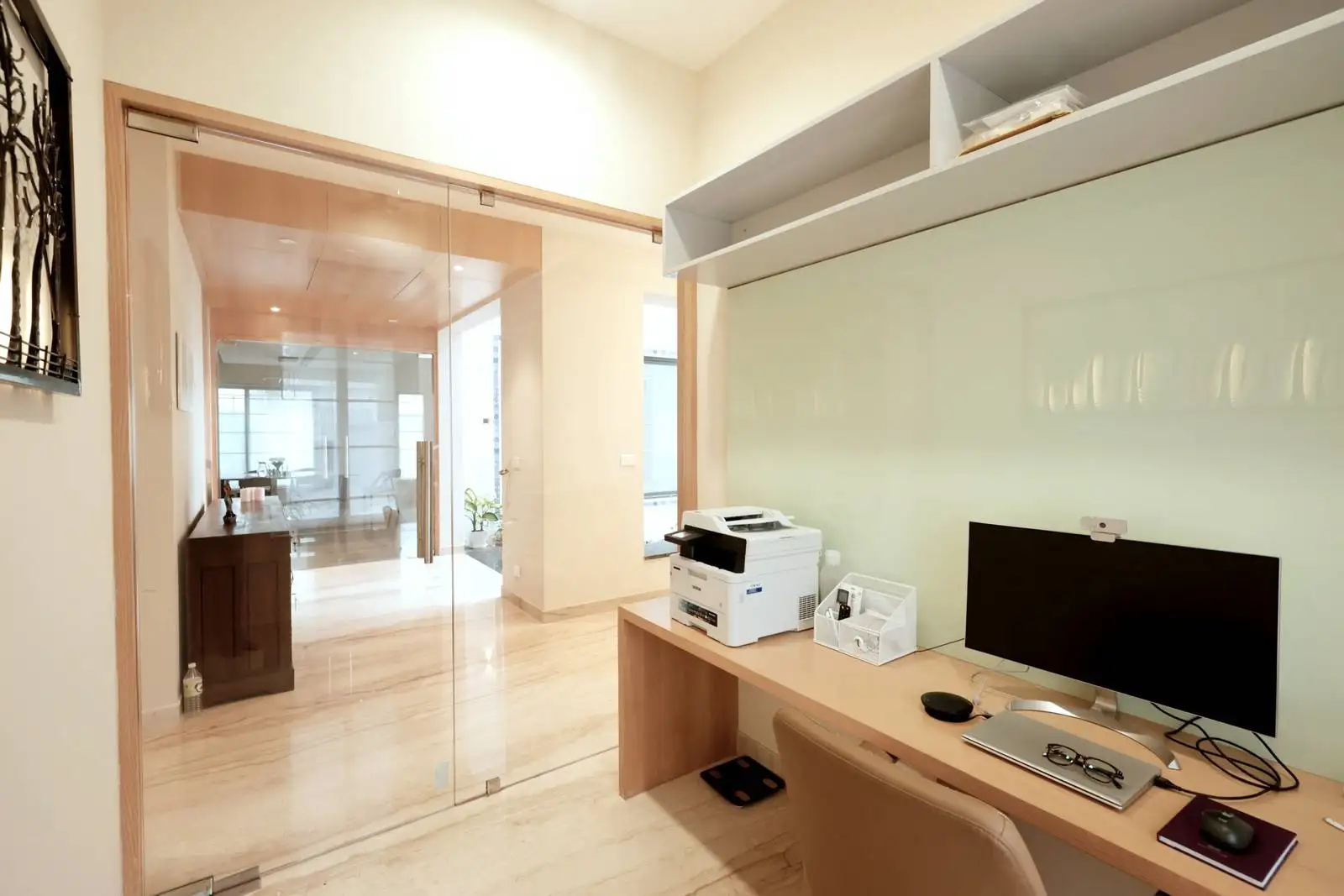 The home office features a streamlined layout with a central wooden desk and glass sliding doors that enhance openness and natural light flow between spaces.