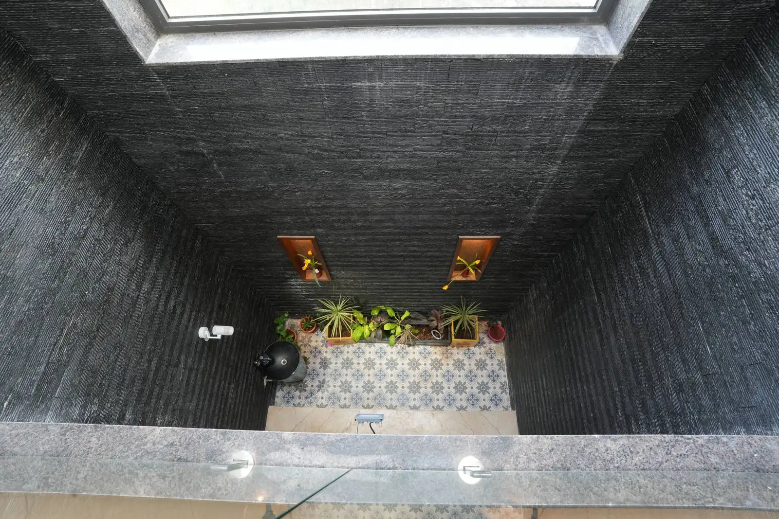 Textured dark walls create an intimate outdoor room, providing a strong backdrop that highlights lighter elements and greenery.