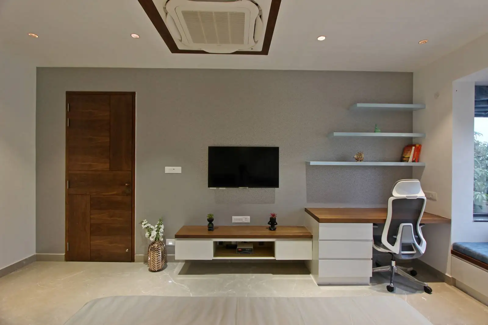 The workspace features a thoughtfully designed wall with integrated floating shelves and a large window seat.