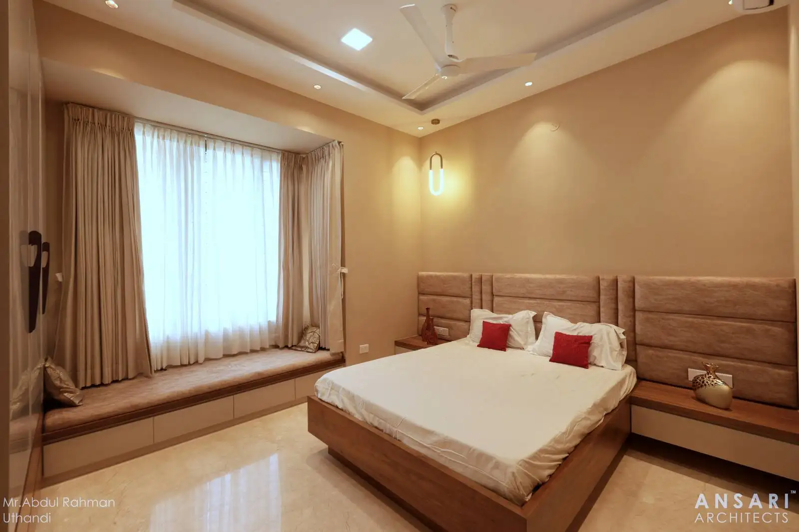 The bedroom features a large bed with a padded headboard, positioned against a feature wall.
