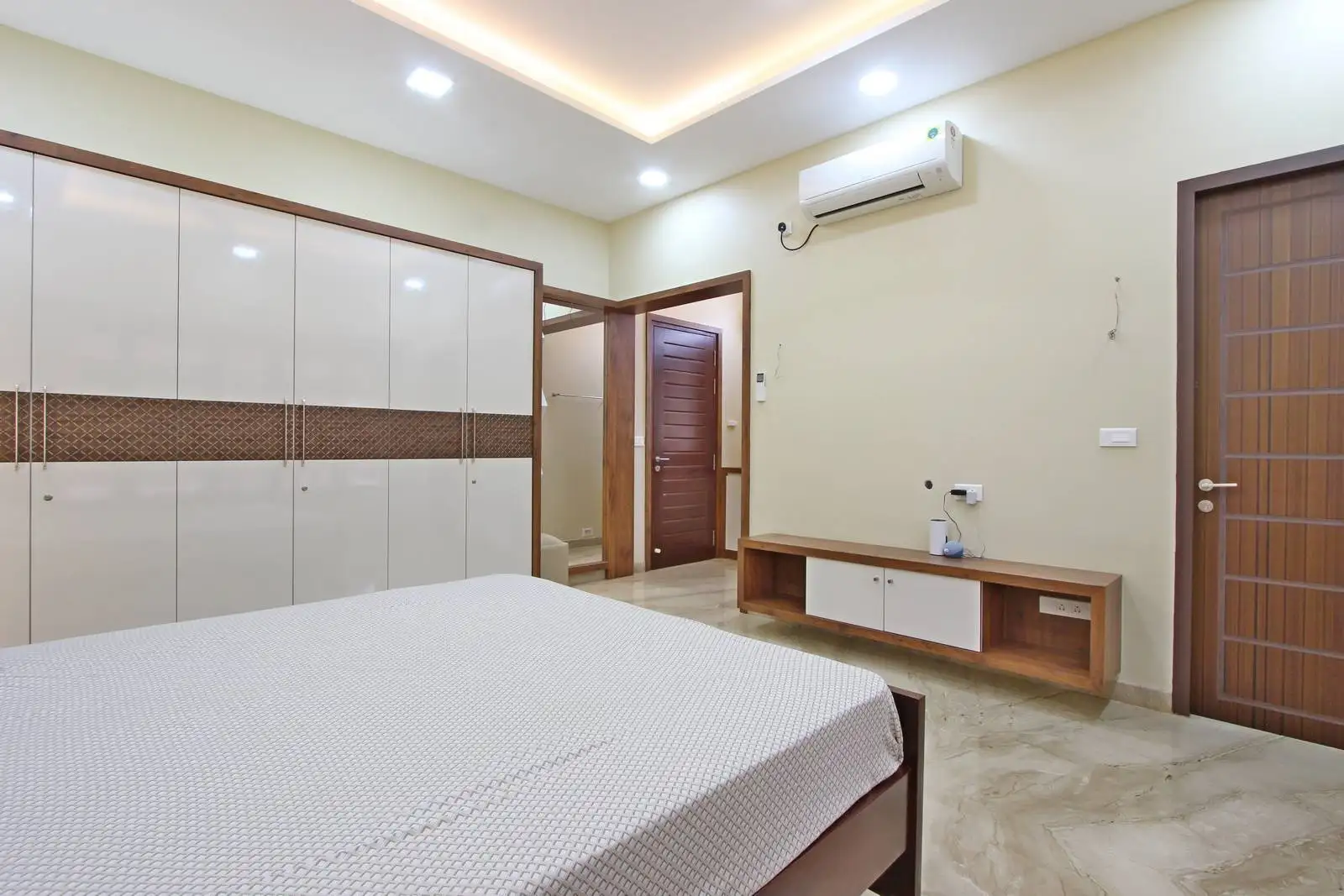 Efficiently organized bedroom with a built-in wardrobe, TV console, and attached bathroom, offering clear circulation and optimized daily functionality.