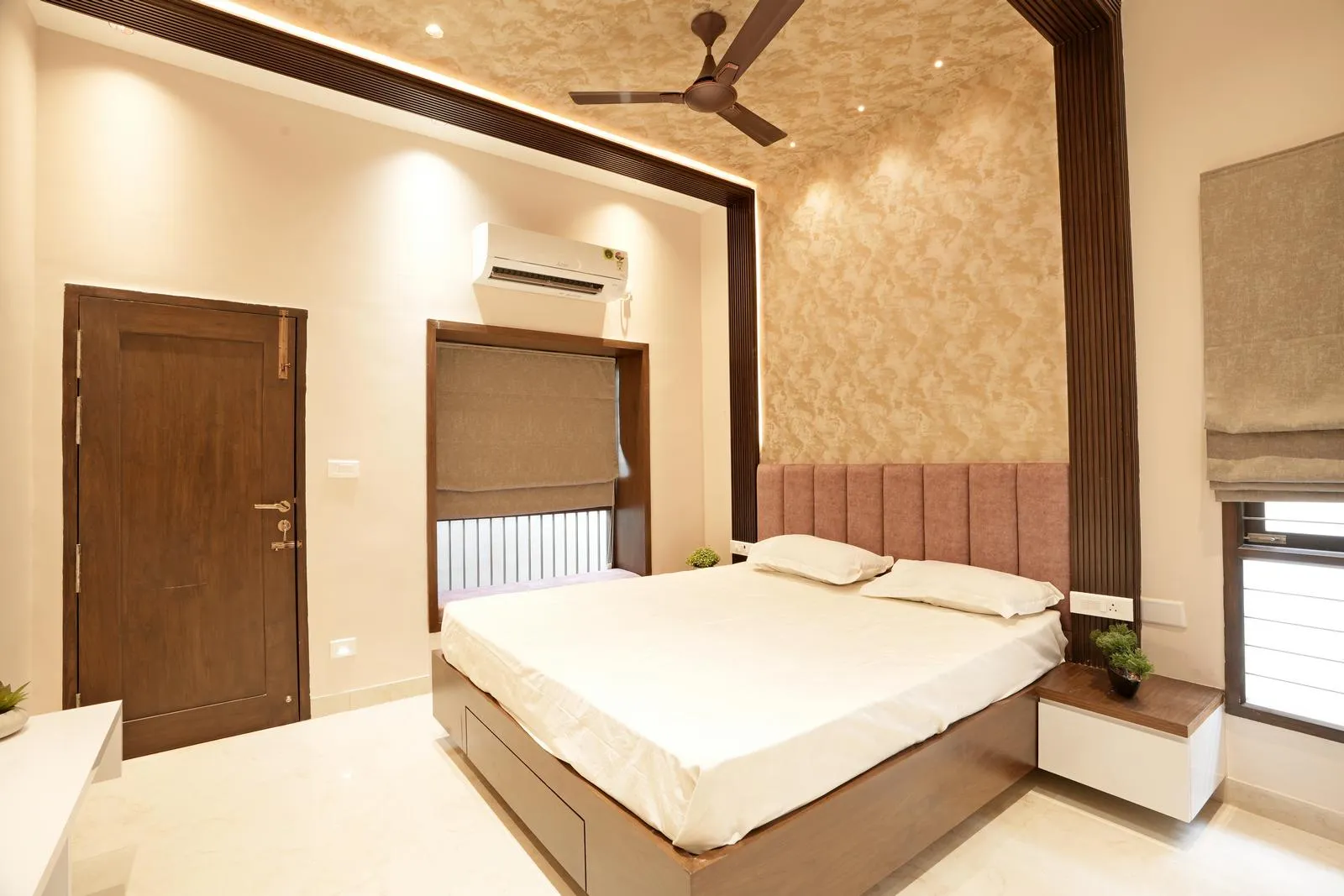 Daughter’s Bedroom ( 12'0" x 14'0" sq.ft ) features a centrally positioned bed against a textured mauve feature wall, polished cream marble flooring, and warm wooden accents. Layered ceiling lighting, integrated nightstands, and neutral window blinds create a bright, balanced, and functional space, designed for comfort, symmetry, and modern aesthetics.