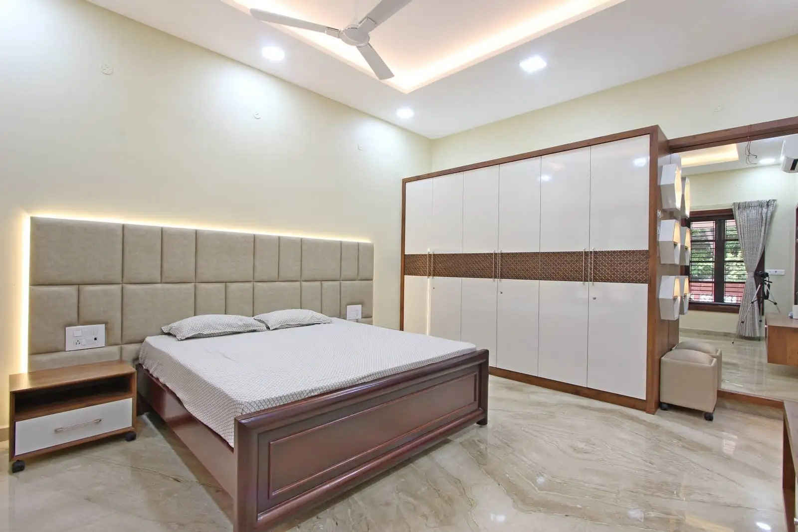 A refined bedroom design combining polished marble flooring, rich wooden furniture, and a modern wardrobe with glossy white and wood finishes. 