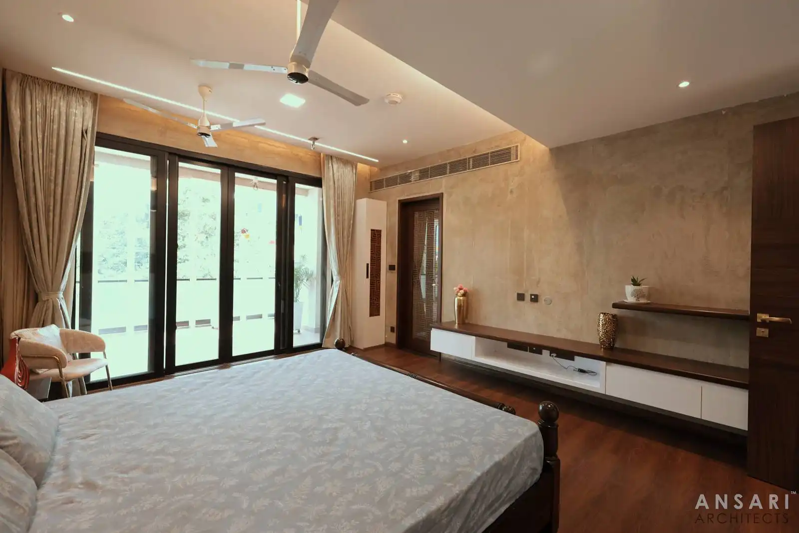 Bedroom design combines comfort and style with a textured feature wall and streamlined built-ins. Neutral tones and polished wood flooring enhance its cozy, refined appeal.