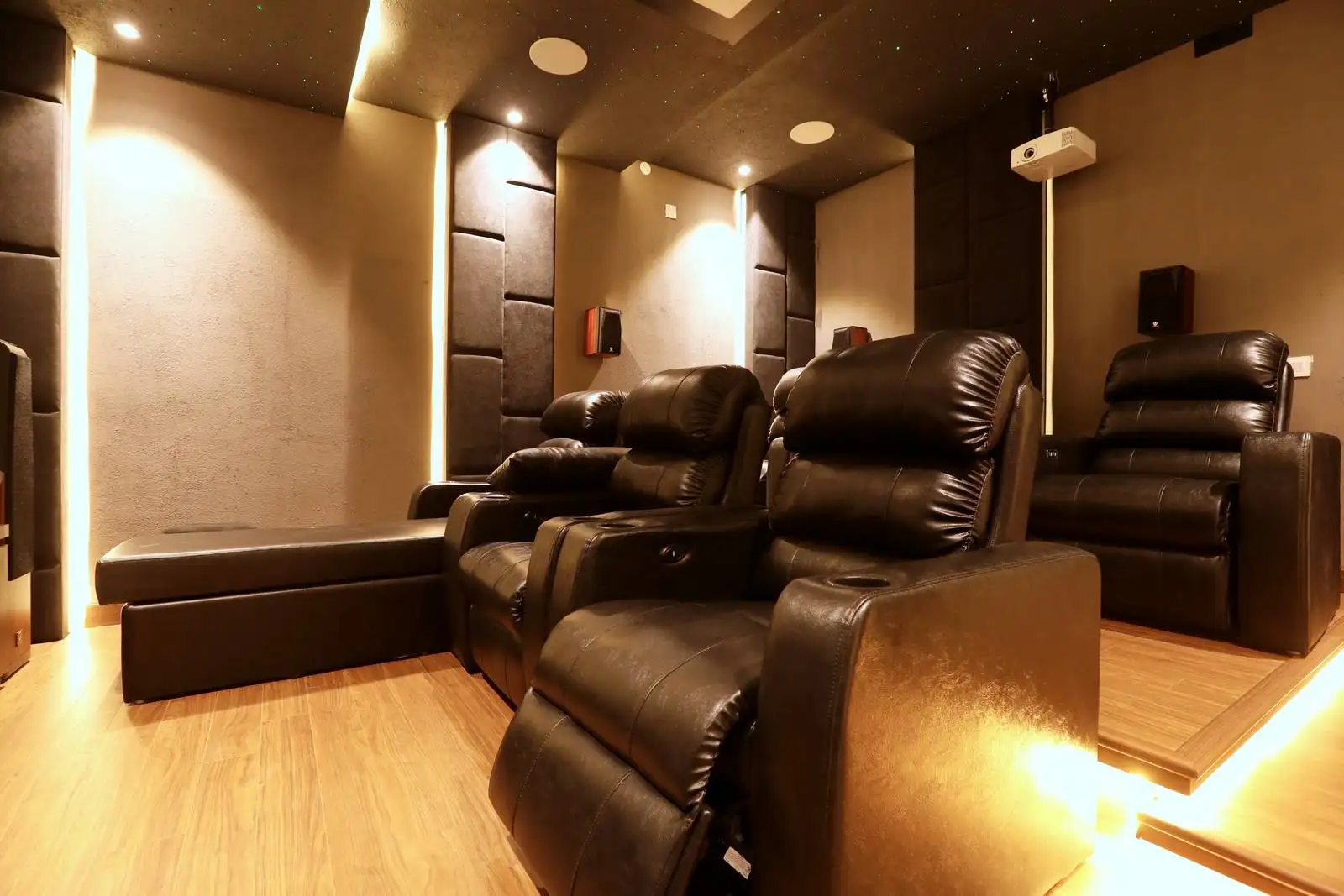 Home theater designed with tiered black leather recliners, warm wood flooring, acoustic wall panels, and subtle ambient lighting for an immersive cinematic experience.