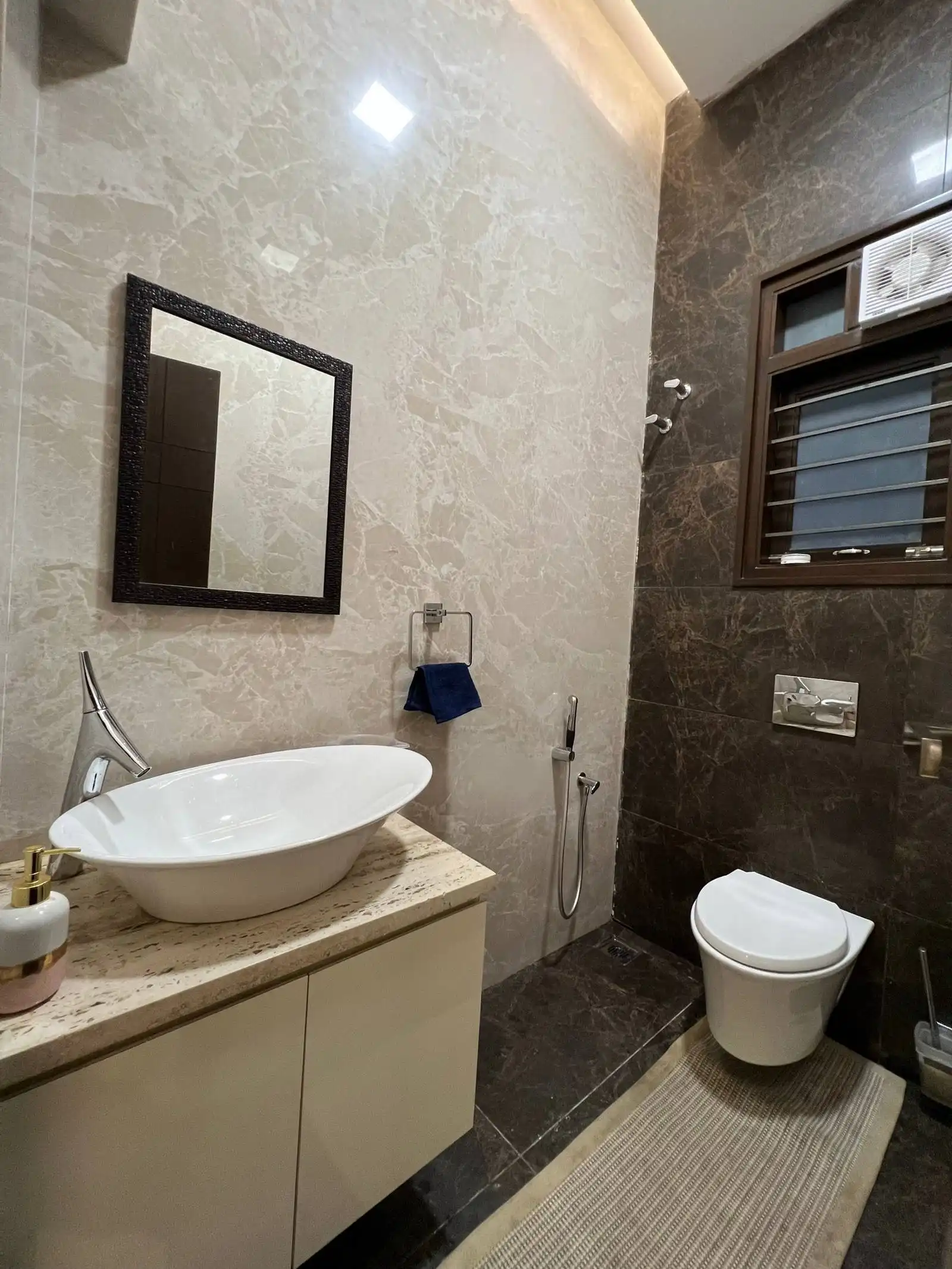 A luxurious bathroom with beige and dark marble walls, a white oval basin on a beige countertop, and a striking black-framed mirror for elegant contrast.