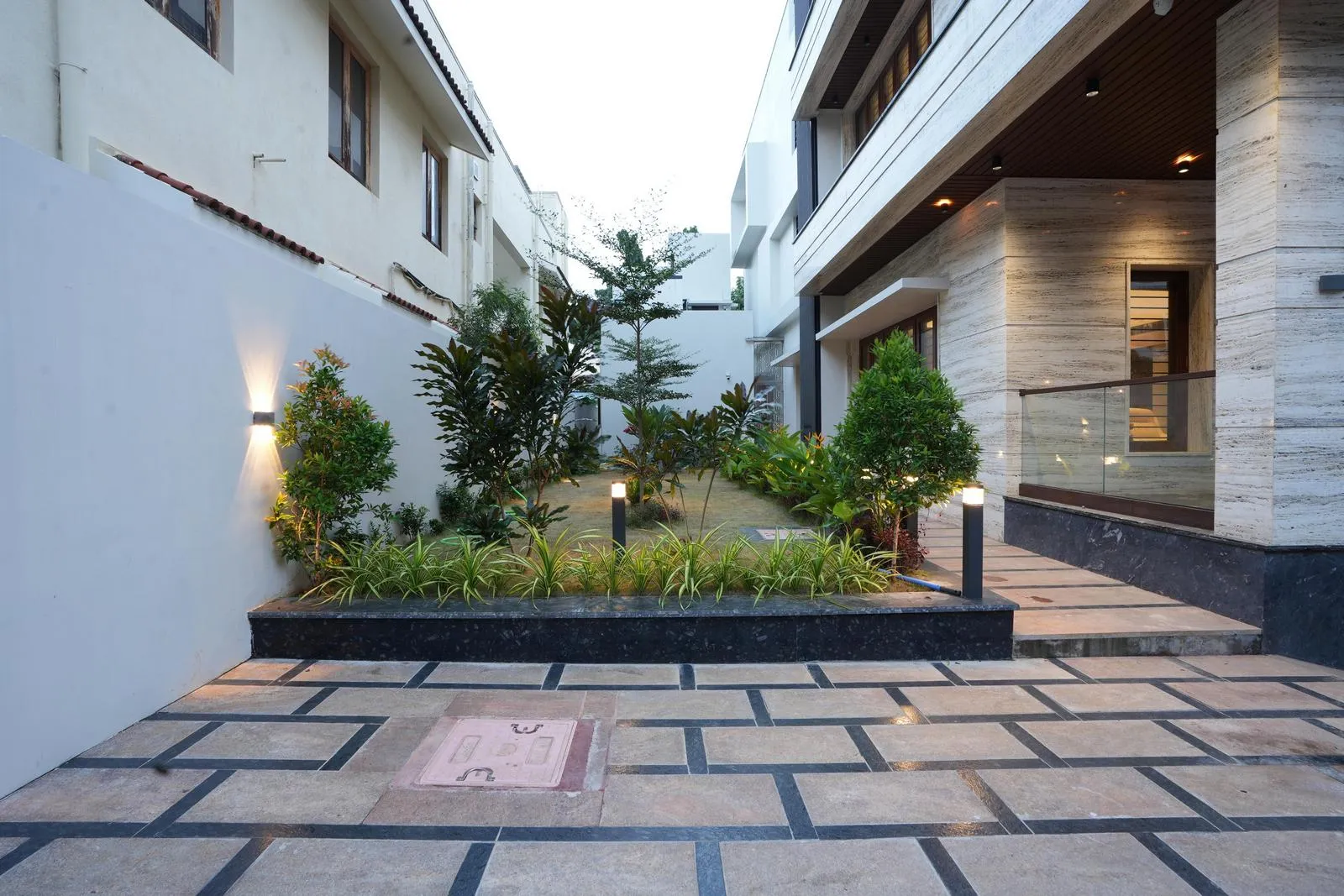 The garden forms a linear courtyard with geometric pathways and raised planters, while an open rear lawn adds depth and a sense of spaciousness.
