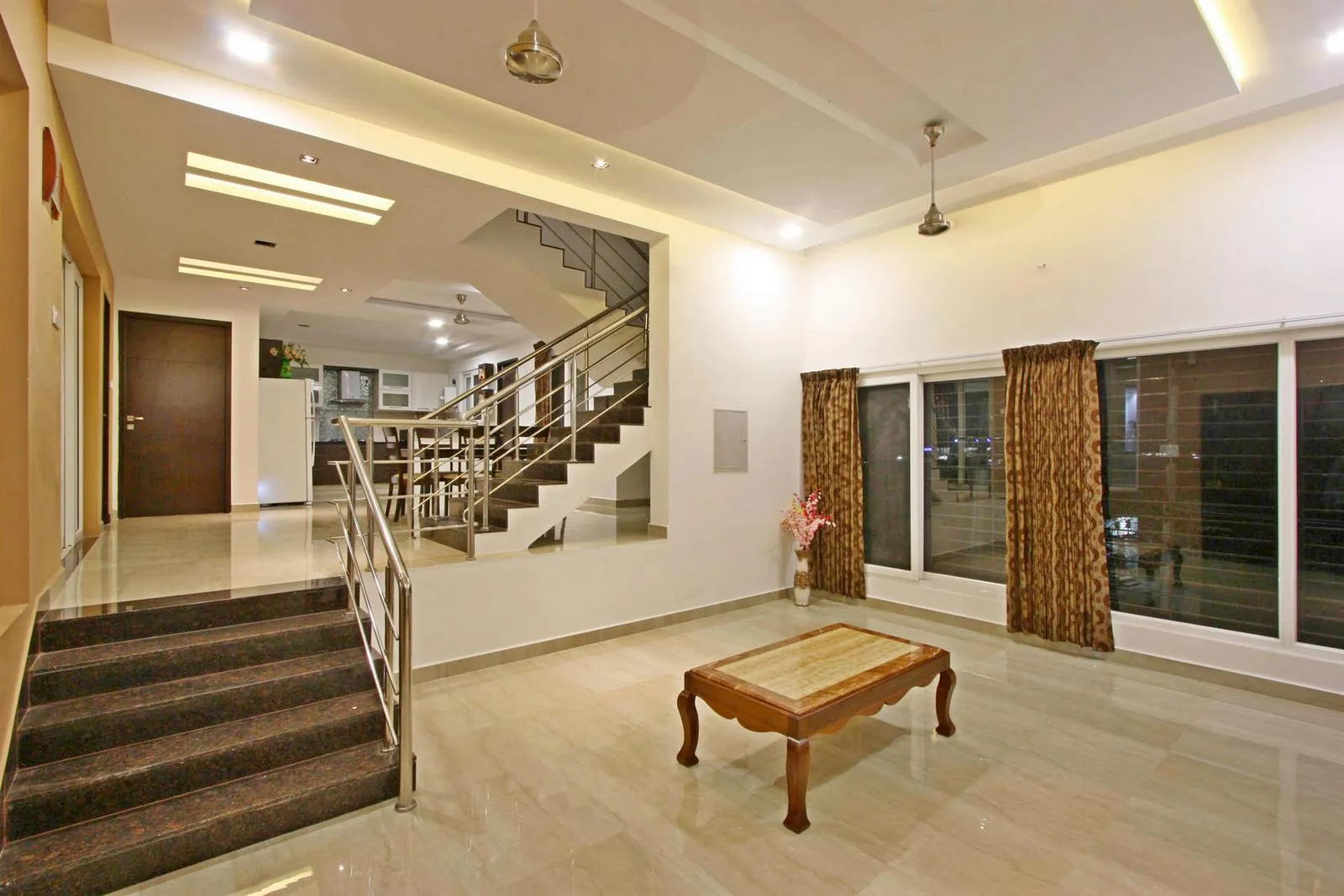 The double-height living area seamlessly connects the entrance, staircase, and upper level, with the central staircase serving as a sculptural anchor. Natural light, a neutral palette, and minimal detailing enhance openness, while carefully selected materials and lighting create a modern, warm, and elegant interior.