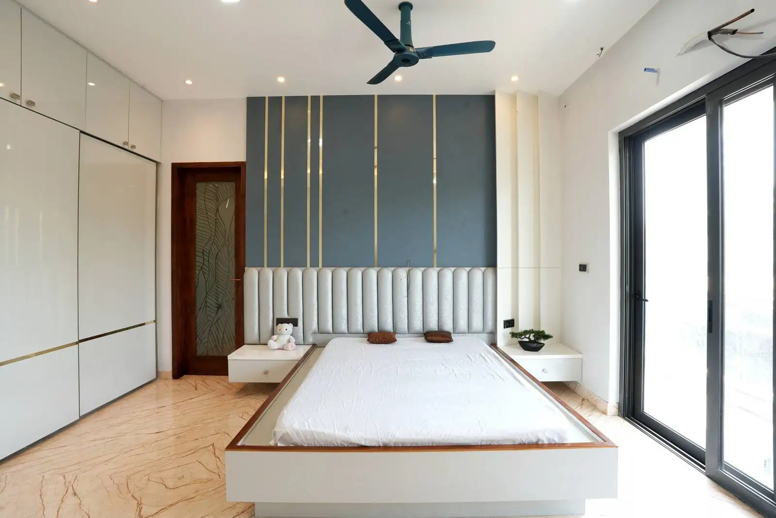 The headboard and decorative wall panels complement large sliding glass doors that flood the room with natural light and open to a balcony.