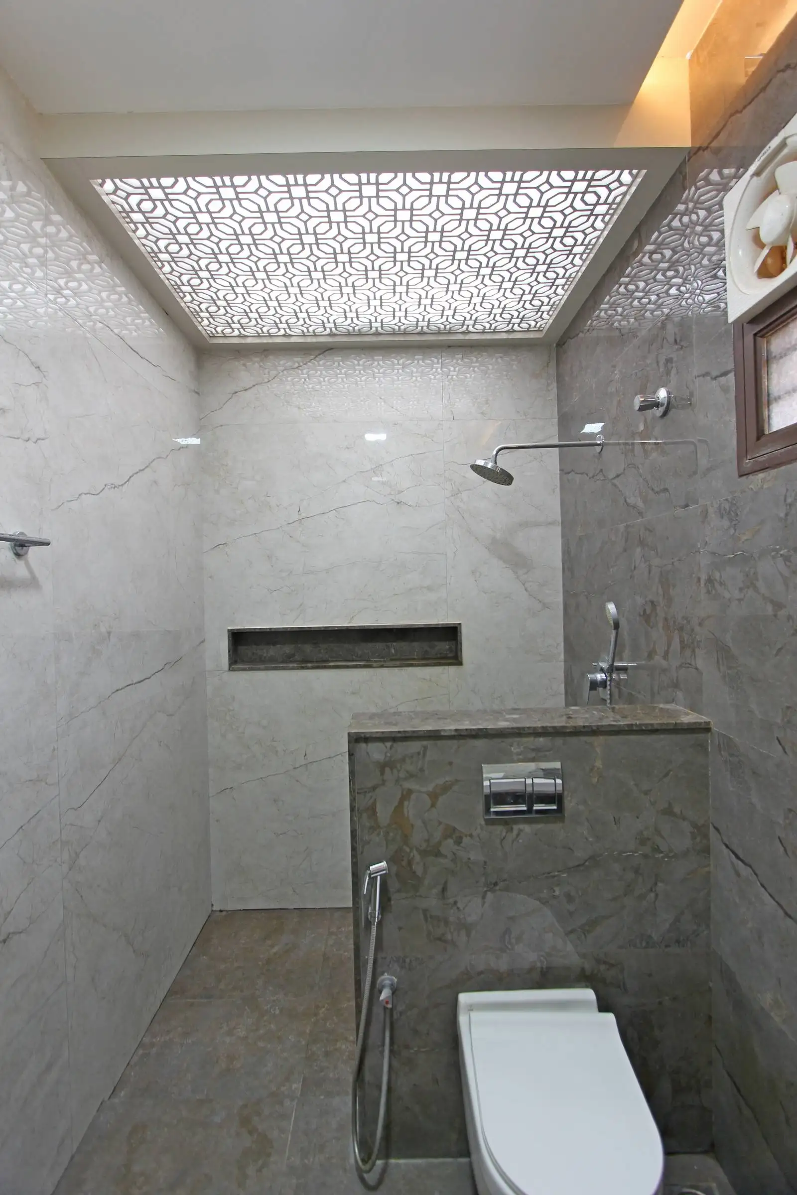Bathroom featuring marble finishes, wall-mounted shower, built-in shelf, and ambient lighting with a decorative ceiling panel for a stylish, functional space.