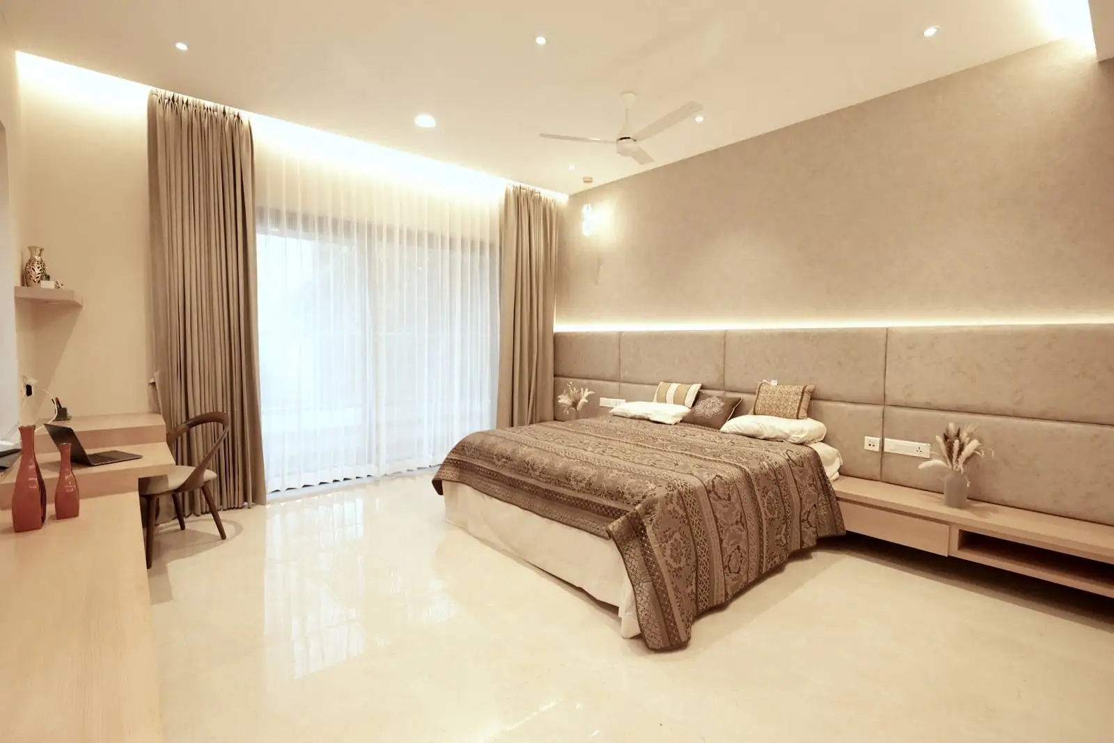 A large window with sheer curtains fills the bedroom with natural light, while cove lighting behind the headboard creates a soft, inviting glow for a calm and serene ambiance.