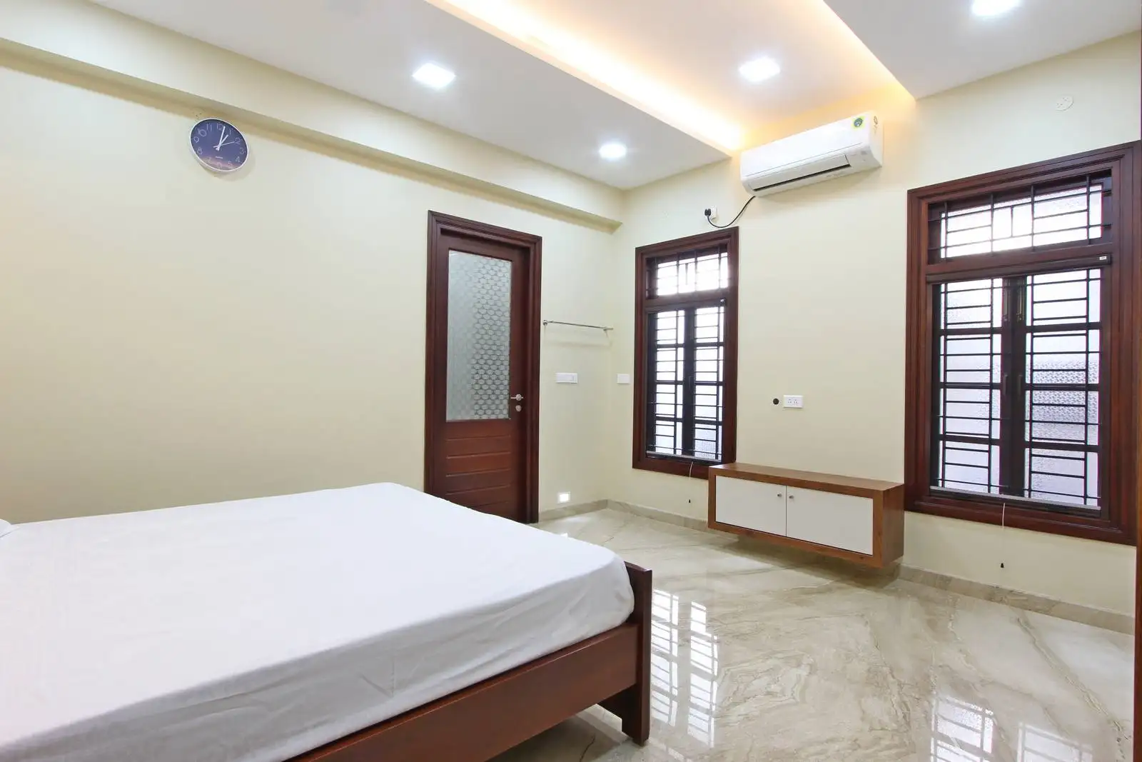 The white walls create a bright, airy, and spacious feel, while wooden elements in the bed, window frames, and doors add warmth and natural texture.