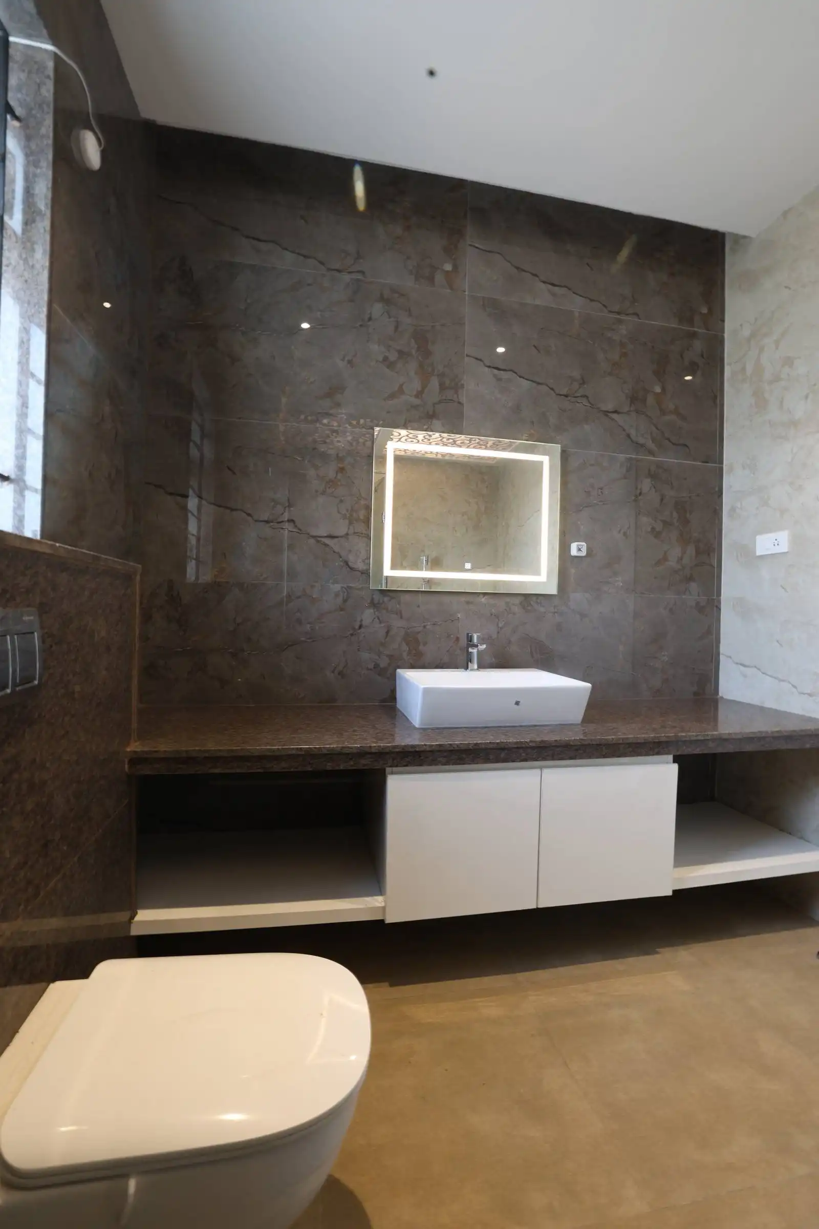 A marble countertop with an inset sink, a wall-mounted illuminated mirror, and a sleek white toilet combine elegance and functionality.