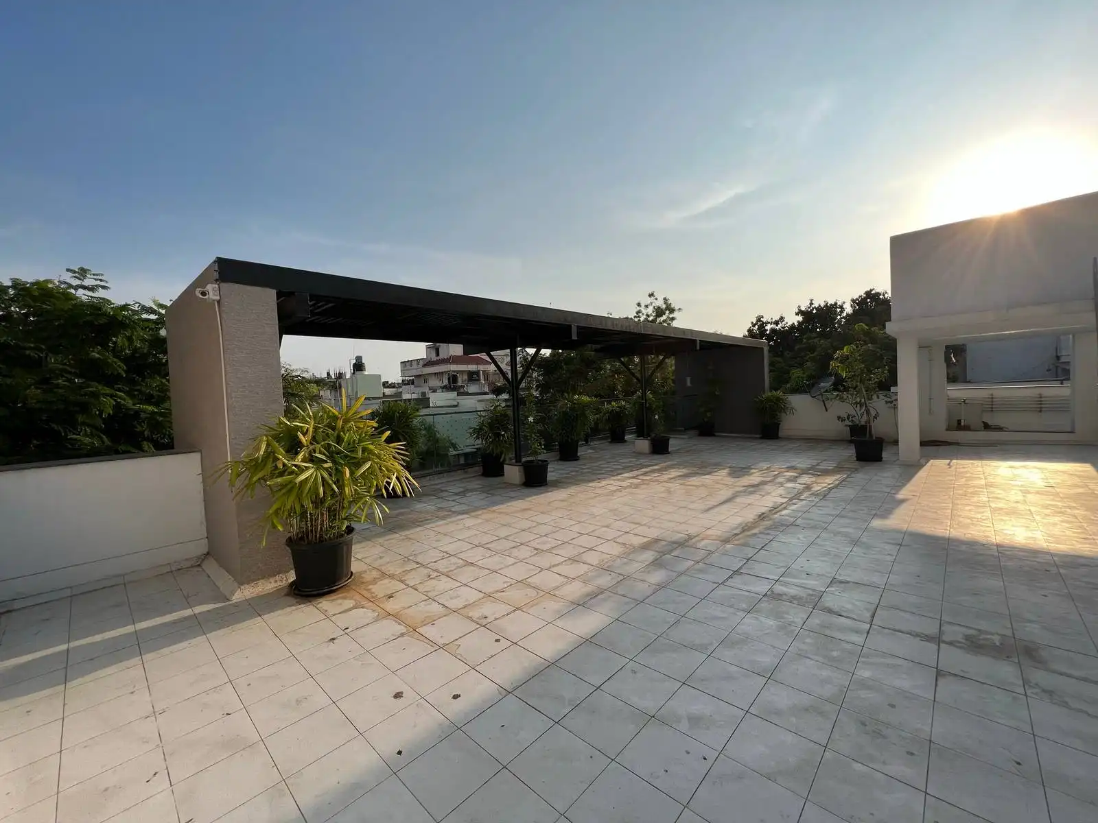 An expansive terrace with light-tiled flooring, a sleek metal-roofed shaded zone, open views, and lush potted greenery for relaxation and gatherings.