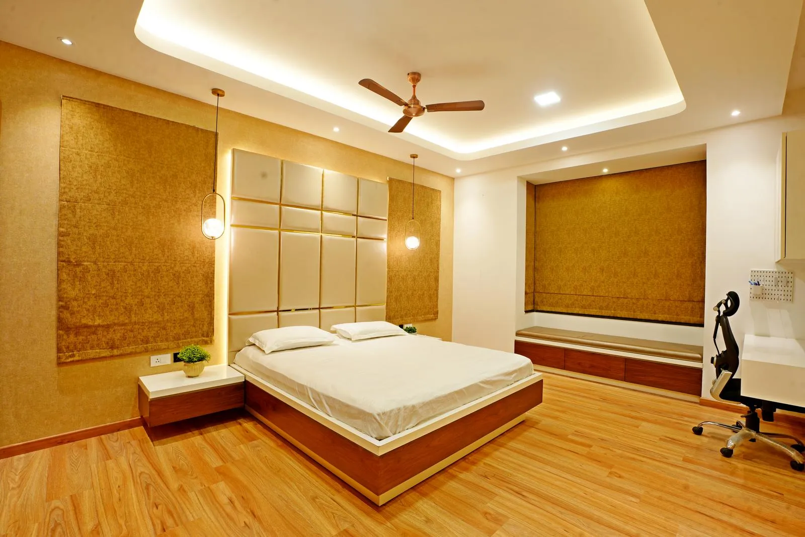 The bedroom (18'0" x 13'6") is open and symmetrical, with a central bed, window seating nook, and integrated study desk for balanced functionality. Warm beige walls, natural wood flooring, and padded headboard panels create a cozy, modern, and elegant space.