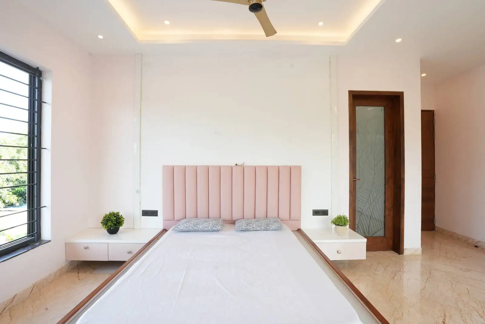 A tall blush pink padded headboard with vertical detailing adds comfort and a soft focal point to the bedroom.