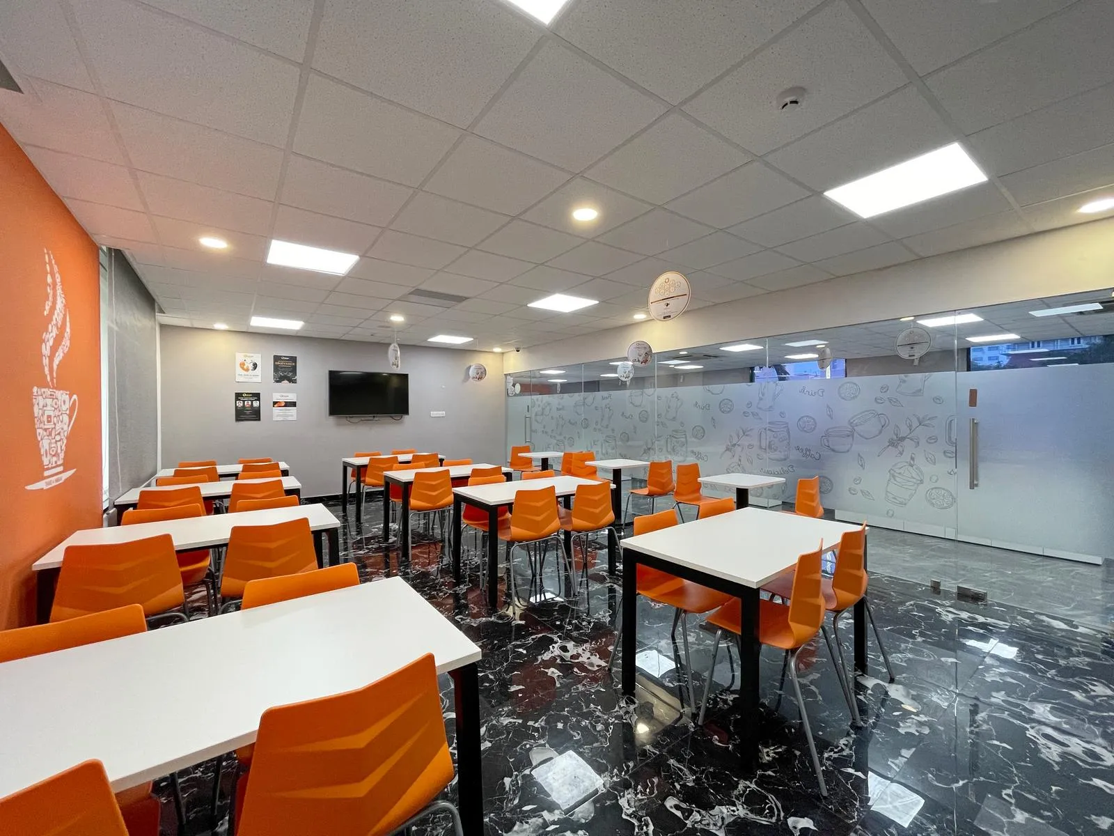 Designed for 42 users, this multipurpose space combines bright orange chairs, white laminate tables, and frosted glass partitions to create an energetic, modern atmosphere. Thoughtful acoustics, lighting, and storage solutions enhance comfort, functionality, and spatial clarity.