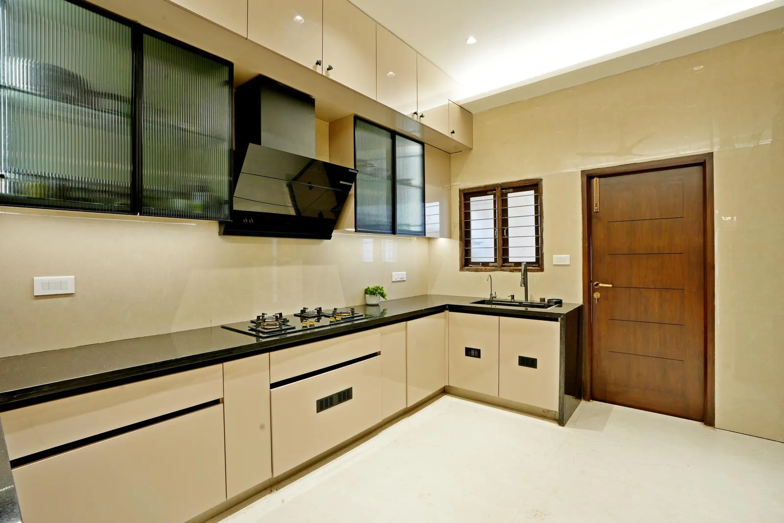 Kitchen ( 12'0" x 13'0" sq.ft ) is planned with a parallel U-shaped layout to ensure an efficient cooking workflow and seamless access to the utility area. Gloss beige cabinetry, black granite countertops, fluted glass shutters, and integrated lighting create a clean, functional space with refined modern detailing.