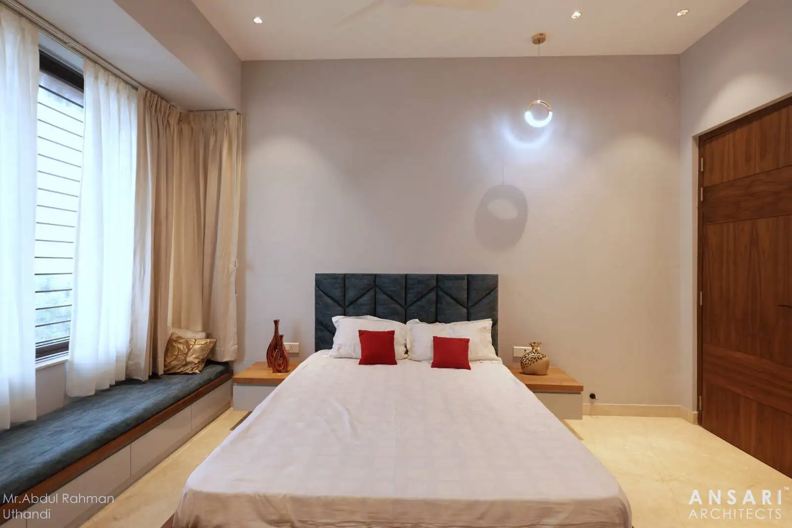 A contemporary bedroom with a blue upholstered bed facing the window, complemented by a dark wood window seat that adds contrast and a cozy spot to enjoy natural light and views.