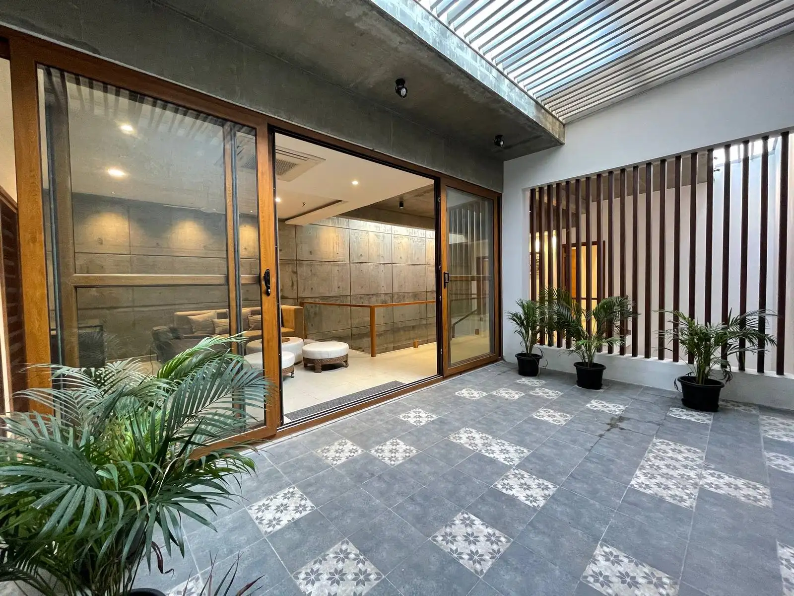 The courtyard uses natural light, ventilation, and textured materials for a calm indoor-outdoor connection. Pergola slats, timber screens, and patterned flooring add rhythm, privacy, and modern tropical style.