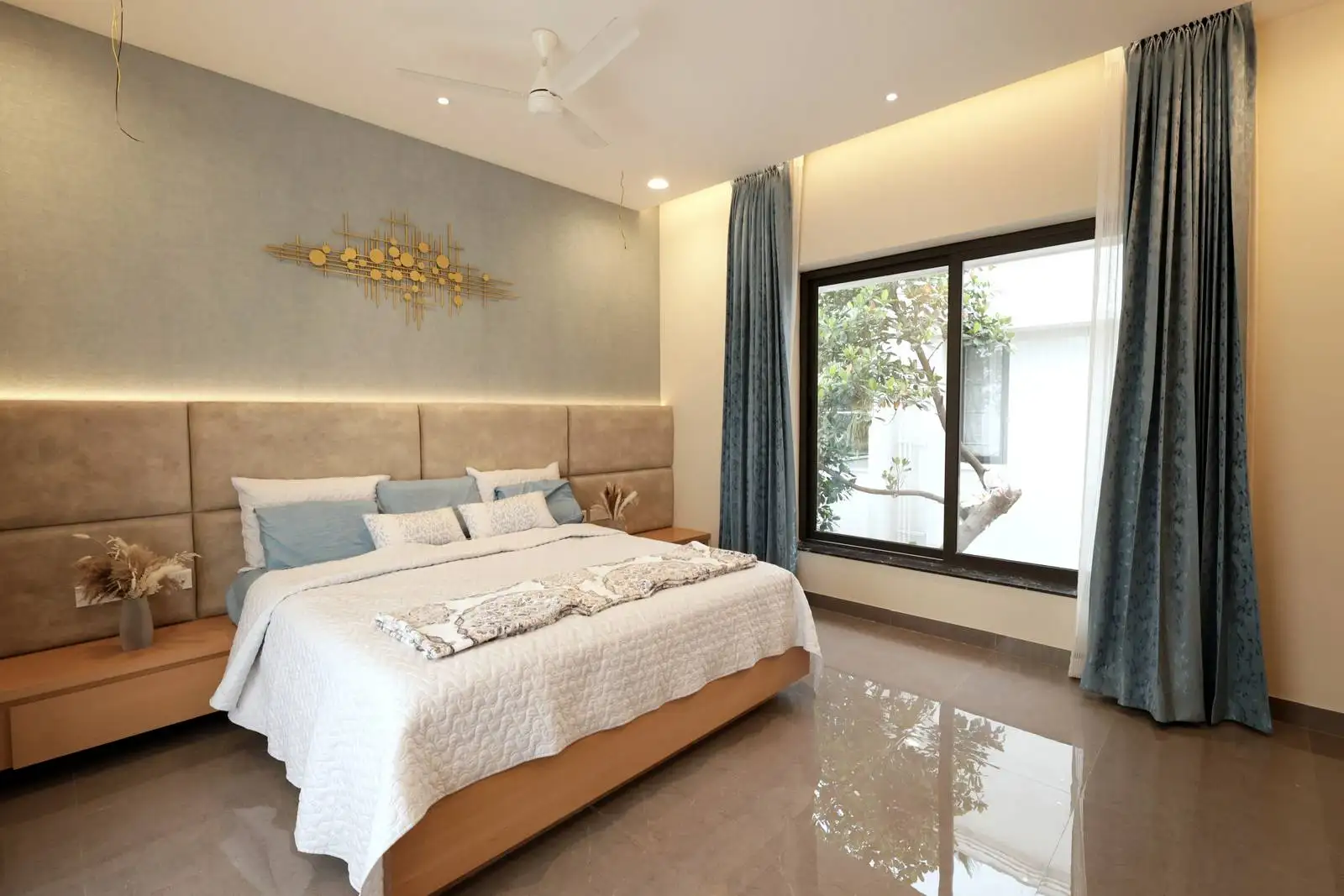 The flooring is a polished, light-colored tile, enhancing the room’s brightness and modern appeal.
The bed and side tables are made of light wood, adding warmth and a natural touch.