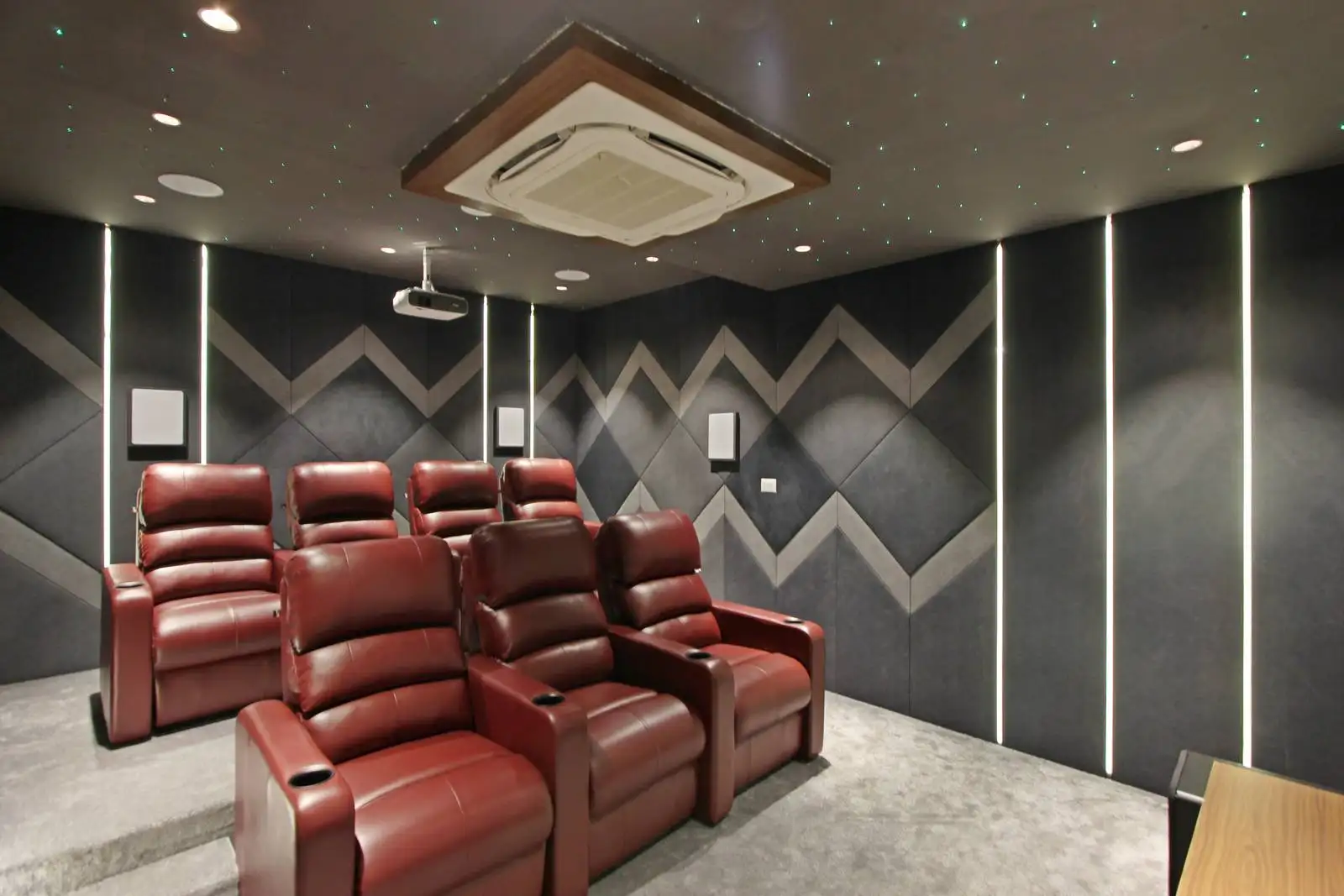 Geometric acoustic wall panels in dark tones provide sound insulation while contributing to a stylish, contemporary home theater design