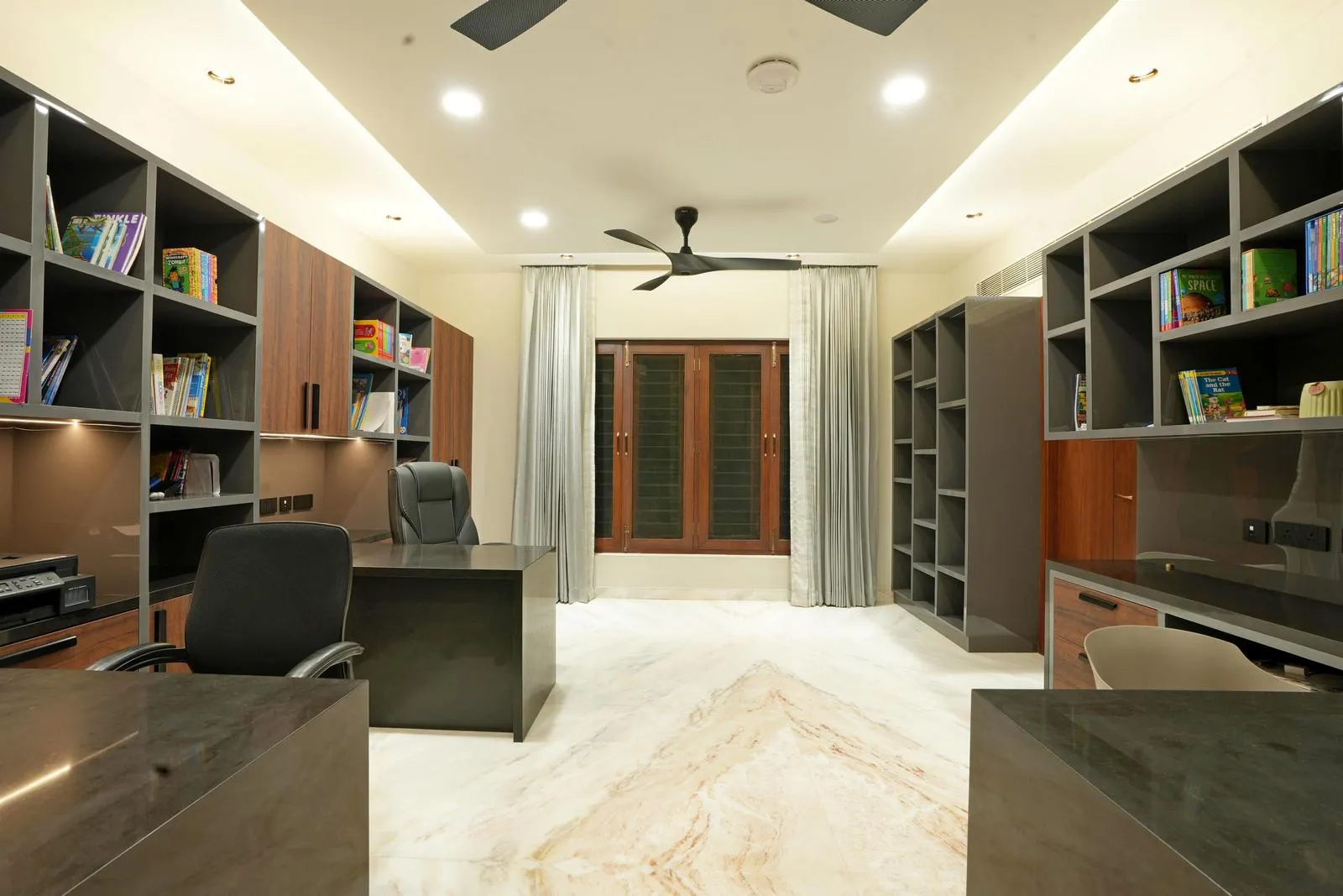 The study has an open central floor for easy movement, while a large window with sheer curtains fills the space with natural light and softens the ambience.